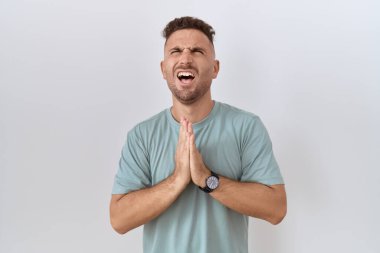 Hispanic man with beard standing over white background begging and praying with hands together with hope expression on face very emotional and worried. begging. 