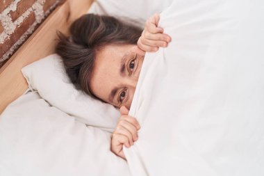 Orta yaşlı bir kadın yatak odasındaki çarşafla yatağa uzanıyor.