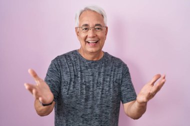 Pembe arka planda gri saçlı orta yaşlı bir adam gülümseyen, yardım eli uzatan ve kabul gören biri.. 