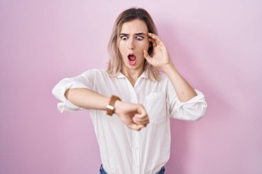 Pembe arka planda duran genç ve güzel bir kadın. Saatine bakıyor. Endişeli, geç kalmaktan korkuyor. 