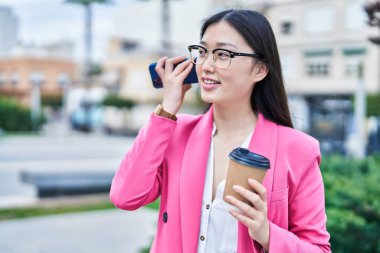 Çinli iş kadını akıllı telefondan sesli mesaj dinliyor parkta kahve içiyor.