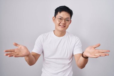 Beyaz arka planda duran Asyalı genç adam gülümseyerek yardım ve kabullenme eli uzatıyor.. 