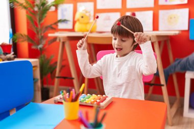 Anaokulunda masada oturmuş ksilofon çalan sevimli beyaz çocuk.