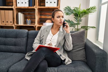 Genç ve güzel İspanyol kadın psikolog psikoloji kliniğinde akıllı telefon okuyarak konuşuyor.