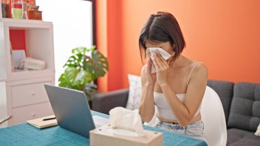 Genç ve güzel İspanyol kadın yemek odasında hapşırırken dizüstü bilgisayar kullanıyor.