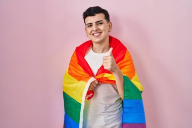 İkili olmayan kişi elinde gökkuşağı lgbtq bayrağı, gülümsüyor mutlu ve pozitif, başparmak yukarıda mükemmel ve onay işareti yapıyor. 