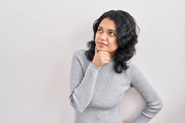 暗い髪を持つヒスパニック系の女性は 質問について考えて顎の手で孤立した背景の上に立って 集中的な表現 思慮深い顔で笑顔 疑わしい概念 — ストック写真