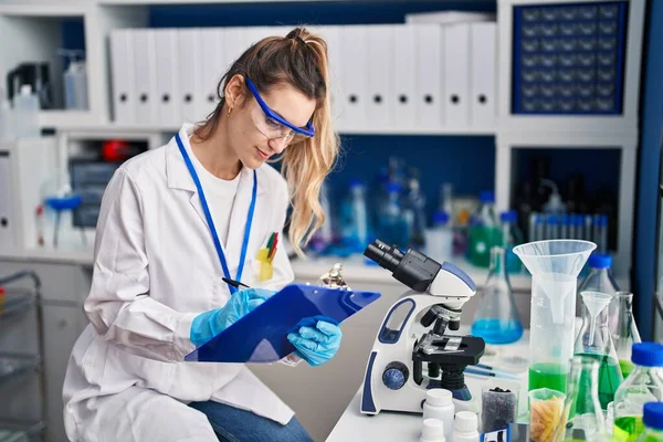 年轻女科学家笑着自信地在实验室写医疗报告 — 图库照片