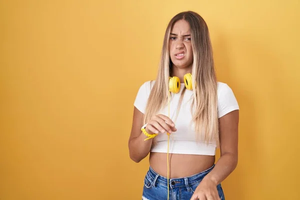 Mladá Blondýnka Stojící Nad Žlutým Pozadím Sluchátkách Znechucený Výraz Nespokojený — Stock fotografie