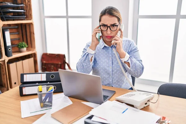 Młoda Latynoska Bizneswoman Pracująca Biurze Rozmawiająca Przez Dwa Telefony Przygnębiona — Zdjęcie stockowe