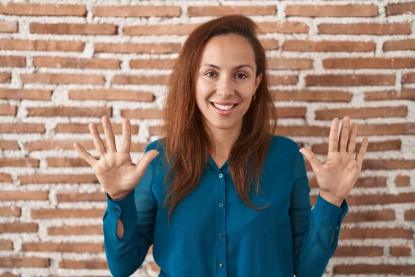 ブルネット女性立ち上がっレンガの壁ショーとポイントアップとともに指番号10ながら笑顔自信と幸せ — ストック写真