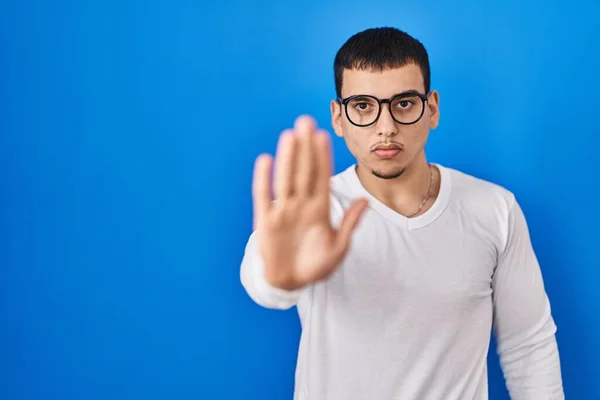 年轻的阿拉伯男子穿着随意的白色衬衫 戴着眼镜 用手拍着手停止歌唱 用消极而严肃的手势警告人 — 图库照片