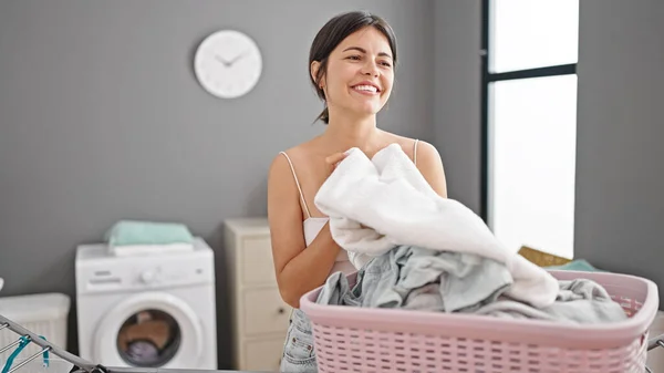 年轻美丽的惊慌失措的女人带着自信的笑容在洗衣房里闻到干净衣服的味道 — 图库照片