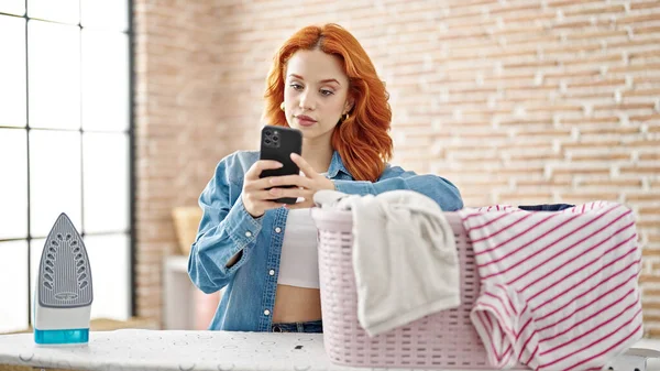 Mujer Pelirroja Joven Usando Teléfono Inteligente Apoyado Tabla Planchar Sala — Foto de Stock