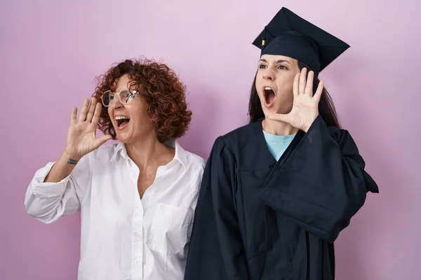 卒業キャップと式のローブを着たヒスパニック系の母親と娘は大声で叫び 口の中で手で横に叫んでいます コミュニケーションの概念 — ストック写真