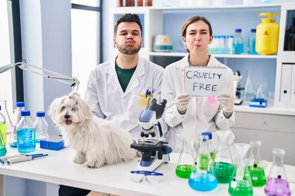 stock image Young hispanic people working at scientist laboratory with dog puffing cheeks with funny face. mouth inflated with air, catching air. 