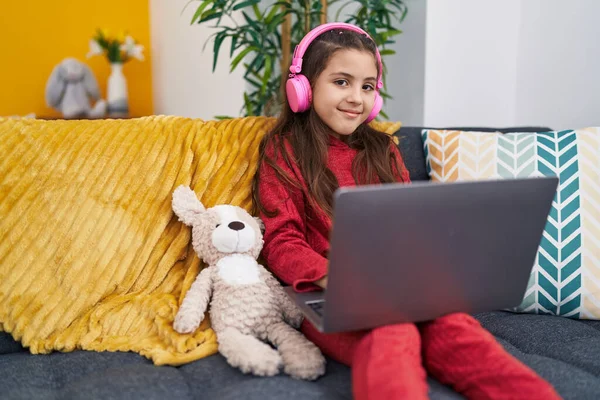 自宅でソファに座ってラップトップとヘッドフォンを使用して愛らしいヒスパニック系の女の子 — ストック写真