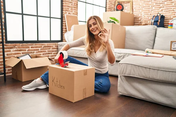 Young Blonde Woman Sitting Floor Closing Boxes Home Doing Sign — Stock Photo, Image