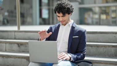 Latin kökenli genç bir iş adamı sokakta oturmuş video görüşmesi yapıyor.