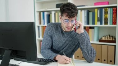 Genç İspanyol öğrenci kütüphane üniversitesinde akıllı telefondan konuşuyor defterde yazıyor.