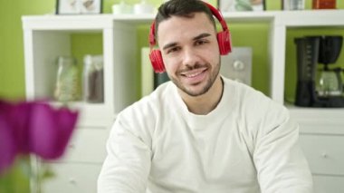 Yemek odasındaki masada dizüstü bilgisayar ve kulaklık kullanan İspanyol genç adam.