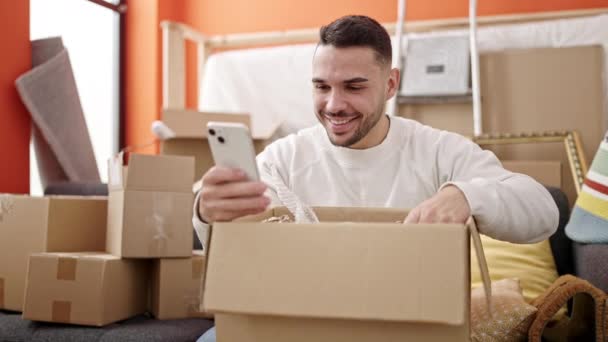 Jovem Hispânico Homem Desempacotar Caixa Papelão Usando Smartphone Nova Casa — Vídeo de Stock