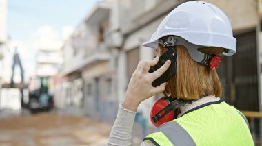 Sarışın genç bir mimar sokakta akıllı telefondan konuşuyor.
