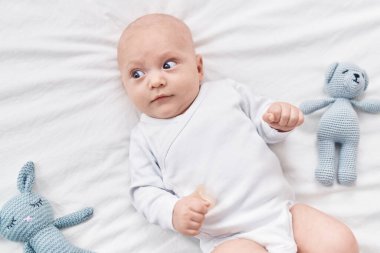 Adorable caucasian baby lying on bed with dolls at bedroom