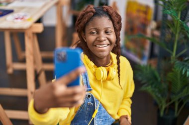 Afrikalı Amerikalı kadın sanatçı, sanat stüdyosunda akıllı telefonla selfie çekiyor.