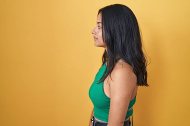 Sarı arka planda duran esmer kadın yan tarafa bakıyor, rahat poz veriyor doğal bir yüz ve kendine güvenen bir gülümseme.. 