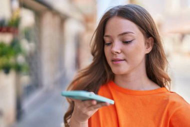 Gülümseyen genç bir kadın caddedeki akıllı telefondan konuşuyor.