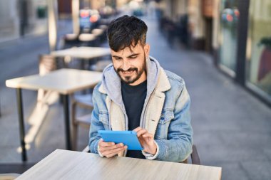 Young hispanic man using touchpad sitting on table at coffee shop terrace
