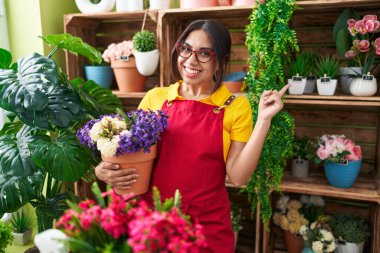 Çiçekçi dükkanında çalışan genç Arap kadın elinde çiçekle mutlu bir şekilde gülümsüyor. 