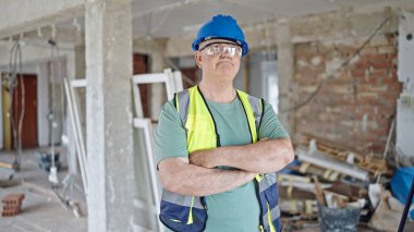 Orta yaşlı, gri saçlı, adam müteahhit. Şantiyede rahat bir ifade ve kollarını kavuşturmuş duruyor.