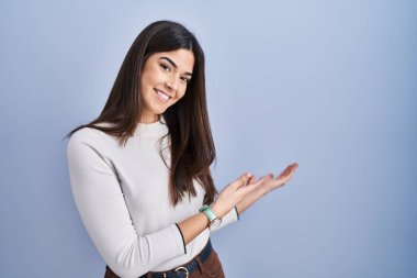 Mavi arka planda duran esmer kadın gülümseyerek doğal bir şekilde içeri girmeye davet ediyor. 