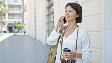Genç, güzel İspanyol kadın turist akıllı telefondan konuşuyor. Sokakta kahve içiyor.