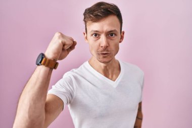 Pembe arka planda dikilen beyaz bir adam öfkeyle bağırırken kızgın ve öfkeli bir şekilde yumruğunu kaldırıyor. öfke ve agresif konsept. 