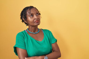 Sarı arka planda duran Afrikalı kadın kollarını kavuşturmuş, ikna olmuş ve kendinden emin bir şekilde yan tarafa bakıyor. 