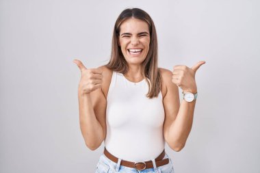 Latin kökenli genç bir kadın beyaz arka plan başarı tabelasının üzerinde duruyor. Elleriyle olumlu jest yapıyor, gülümsüyor ve mutlu. Neşeli ifade ve kazanan jest. 