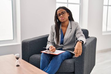 Danışmanlık ofisinde örgü ören Afrikalı genç bir Amerikalı. Uykulu ve yorgun görünüyor. Yorgun ve akşamdan kalma, tembel gözleri var.. 