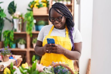 Afrikalı Amerikalı kadın çiçekçi çiçekçiye akıllı telefon kullanarak gülümsüyor.