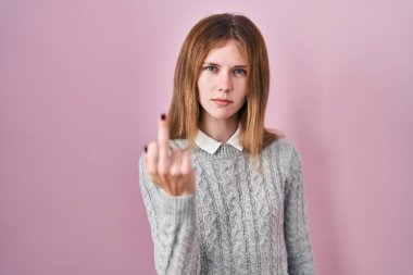 Beautiful woman standing over pink background showing middle finger, impolite and rude fuck off expression 