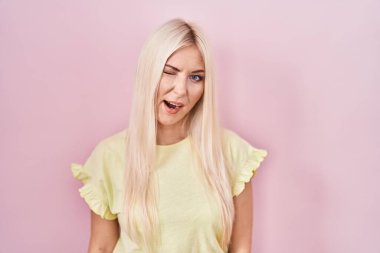 Beyaz bir kadın pembe arka planda durmuş kameraya seksi bir ifadeyle bakıyor, neşeli ve mutlu bir yüzle.. 