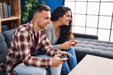 Man and woman couple playing video game sitting on sofa at home