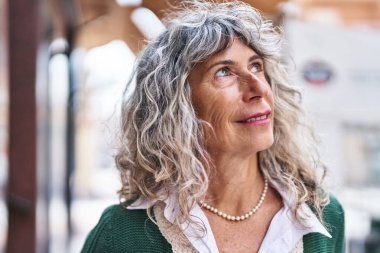 Orta yaşlı bir kadın sokakta kendine güvenerek gülümsüyor.