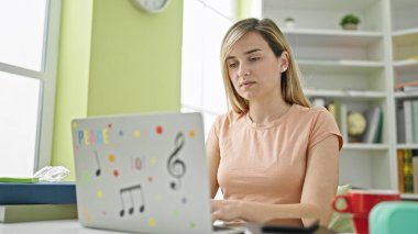 Kütüphanede dizüstü bilgisayar kullanan genç sarışın kız öğrenci.