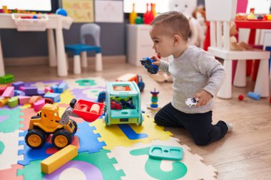 Anaokulunda yerde oturan sevimli İspanyol çocuk araba oyuncağıyla oynuyor.