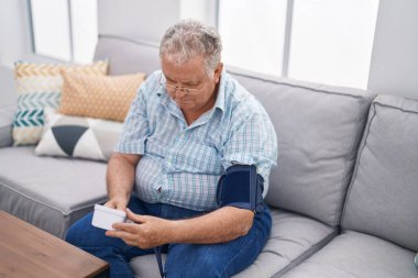 Orta yaşlı, kır saçlı, nabız ölçer kullanan bir adam.