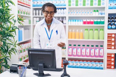 Orta yaşlı Afro-Amerikan kadın eczacı eczanede bilgisayar kullanarak reçete okuyor.