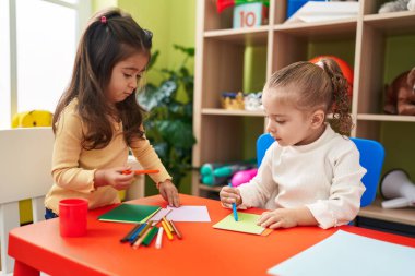 Anaokulunda masa başında oturmuş kağıda resim çizen sevimli kızlar.